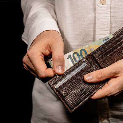Mann hält eine genarbte Ledergeldbörse in braun und zieht einen Geldschein aus dem Scheinfach