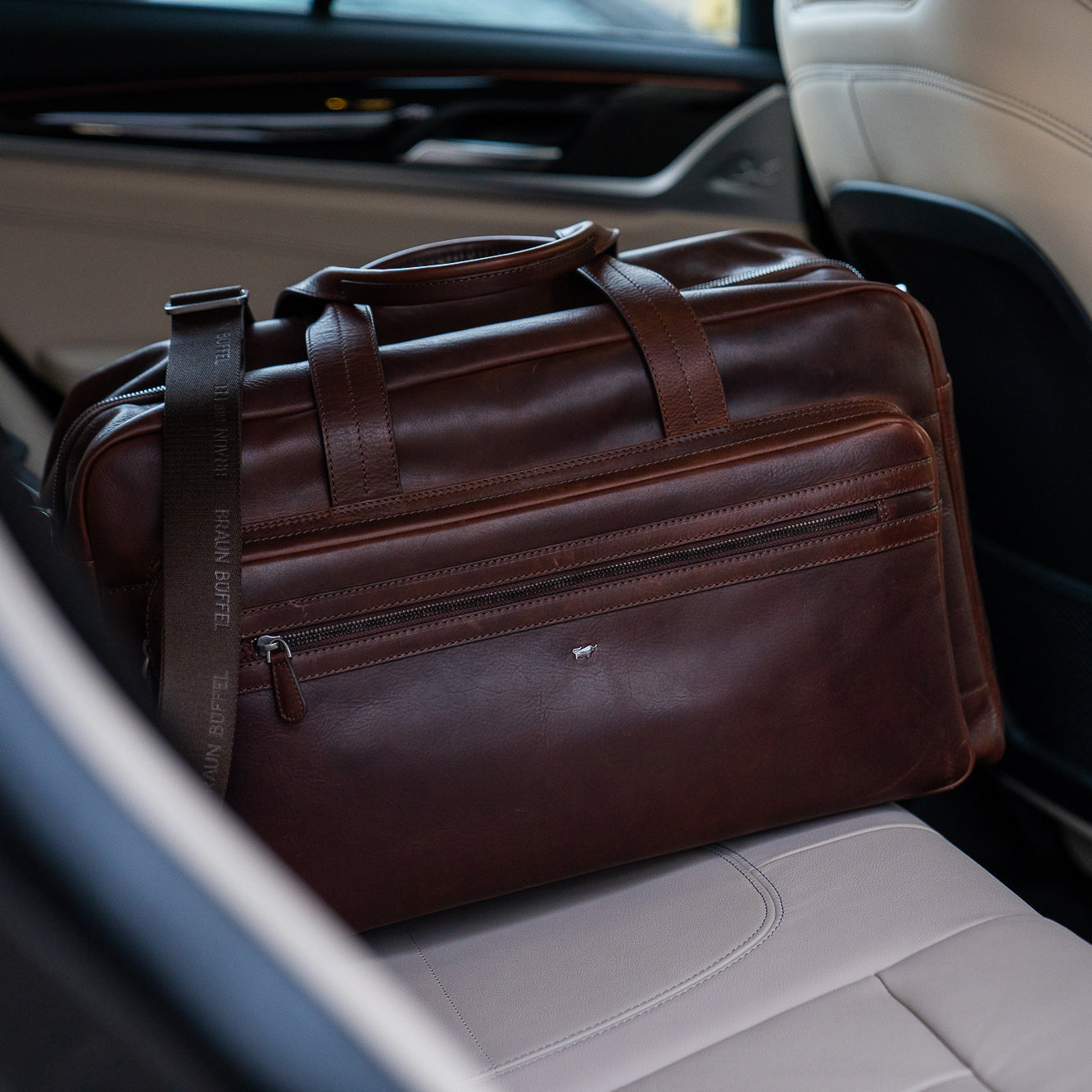 Eine braune Leder-Reisetasche liegt auf der Rückbank eines Autos
