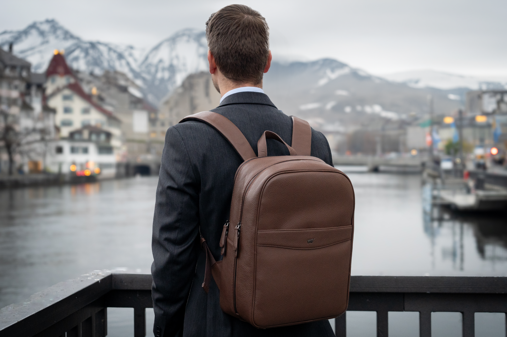 Mann steht mit Lederrucksack in einer winterlichen Landschaft mit Bergen